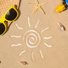 A drawing of the sun on the sand, surrounded by items that people use to protect themselves from UV damage, including sunscreen, a hat, and sunglasses.