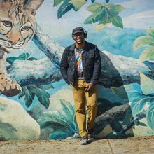 A smiling Black man leans against a colorful wall