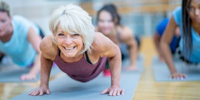 Woman smiling at the camera working out on a blue yoga mat.