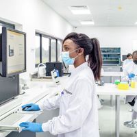 Women looks at computer screen in a lab coat and mask