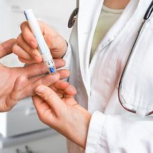 A doctor checking a patient&rsquo;s blood sugar levels using a glucometer on their ring finger.