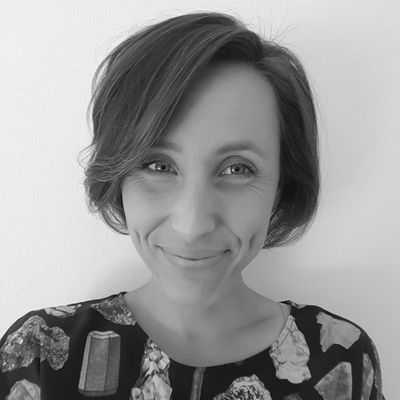 A black and white headshot of a woman in a blouse covered in gems, minerals, and rocks